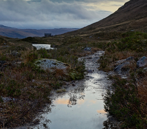The Coire Fionnaraich bothy from a puddle in the path.